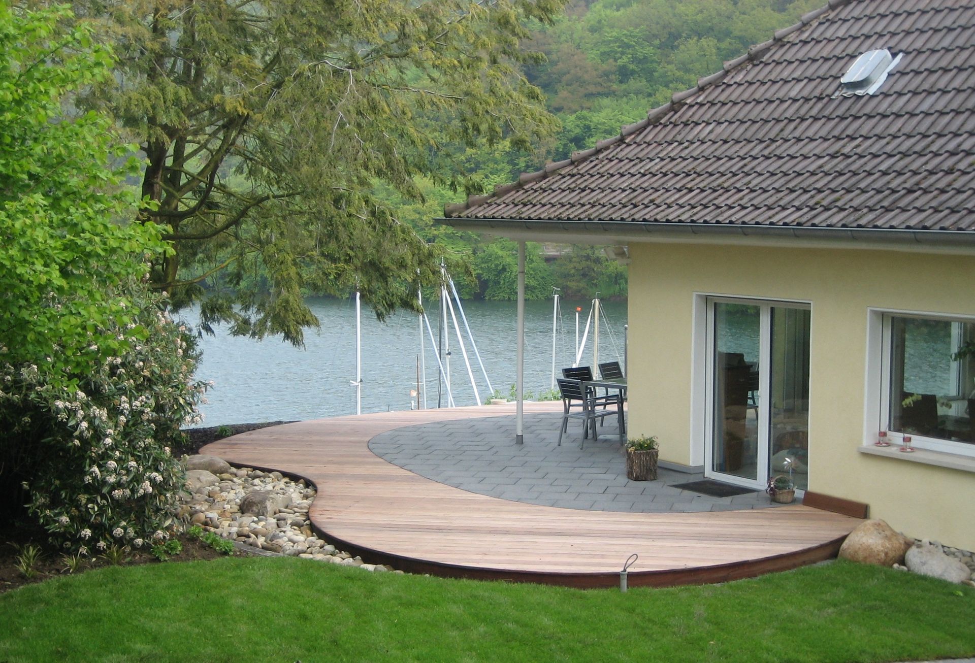 Terrasse mit geschwungenem Holzdeck und Natursteinpflaster am Wasser