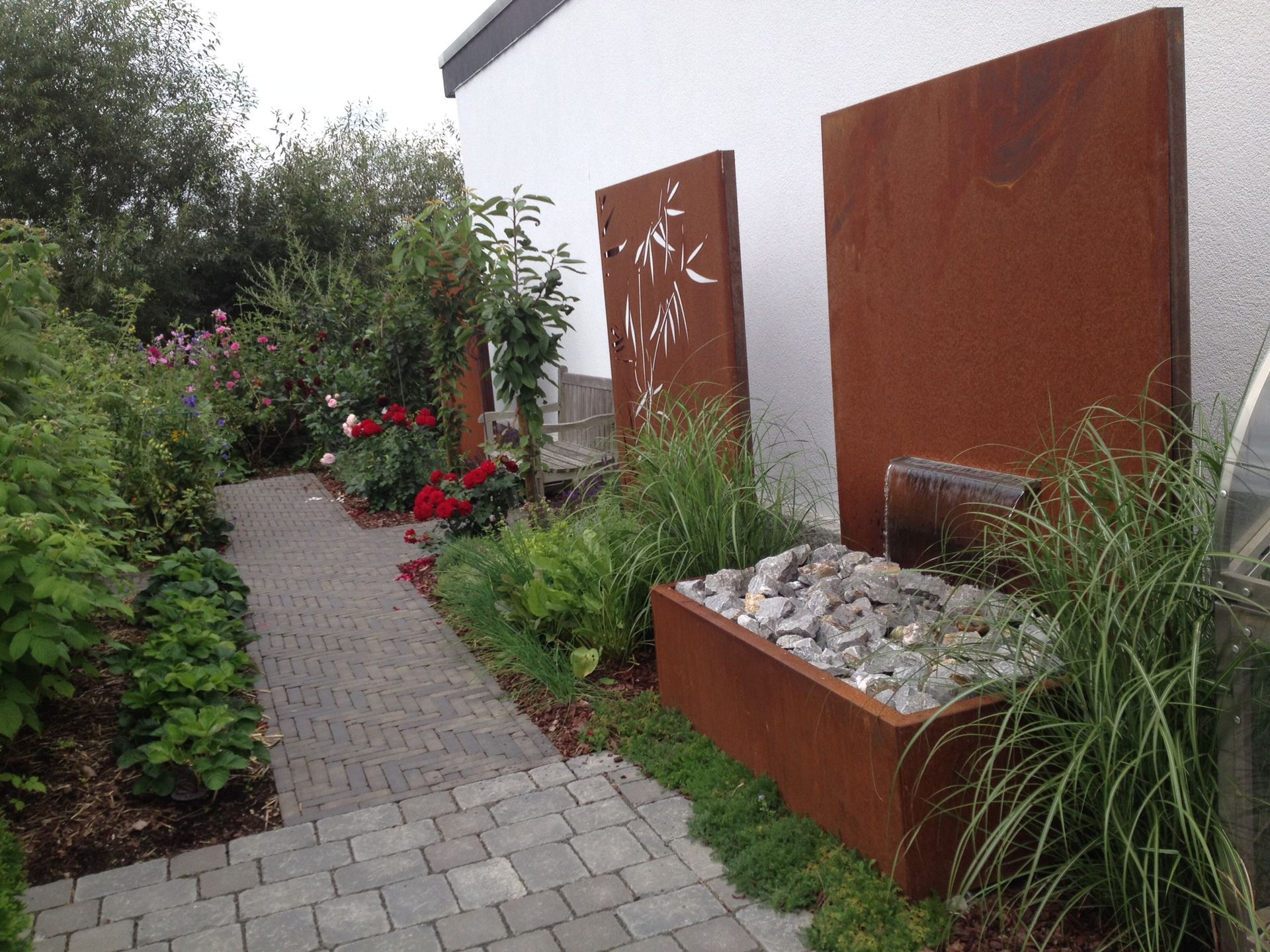 Gepflegter Gartenweg mit Cortenstahl-Wasserspiel und Ziergräsern