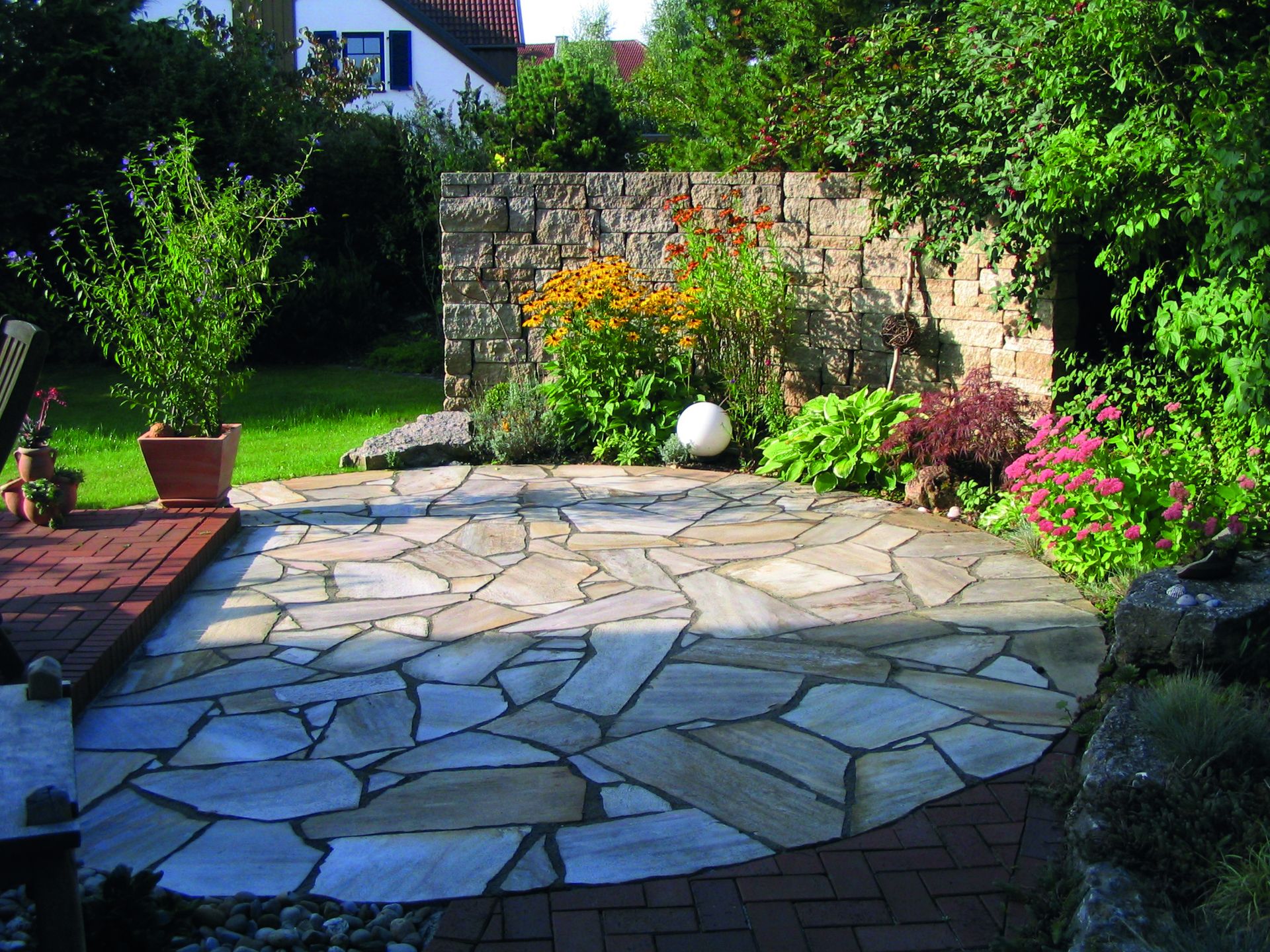 Natursteinterrasse mit Gabionenmauer und sommerlicher Staudenbepflanzung